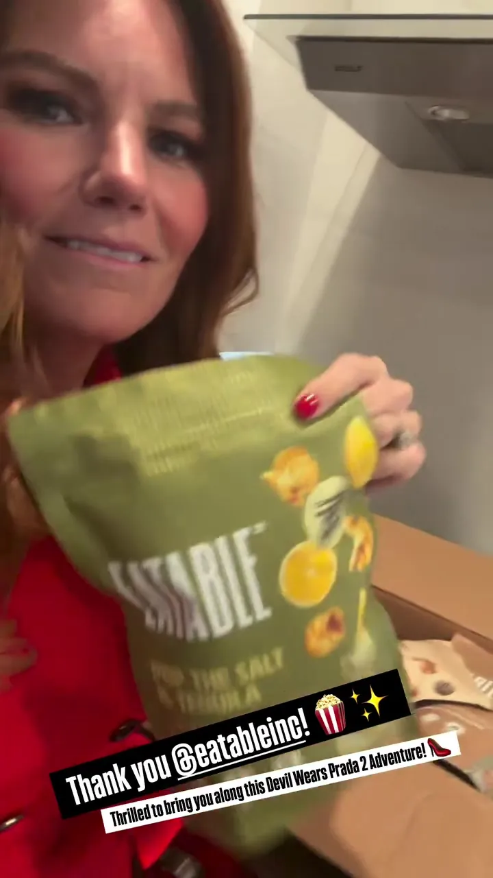Kristin in red holding up a bag of Eatable popcorn from her Devil Wears Prada 2 delivery